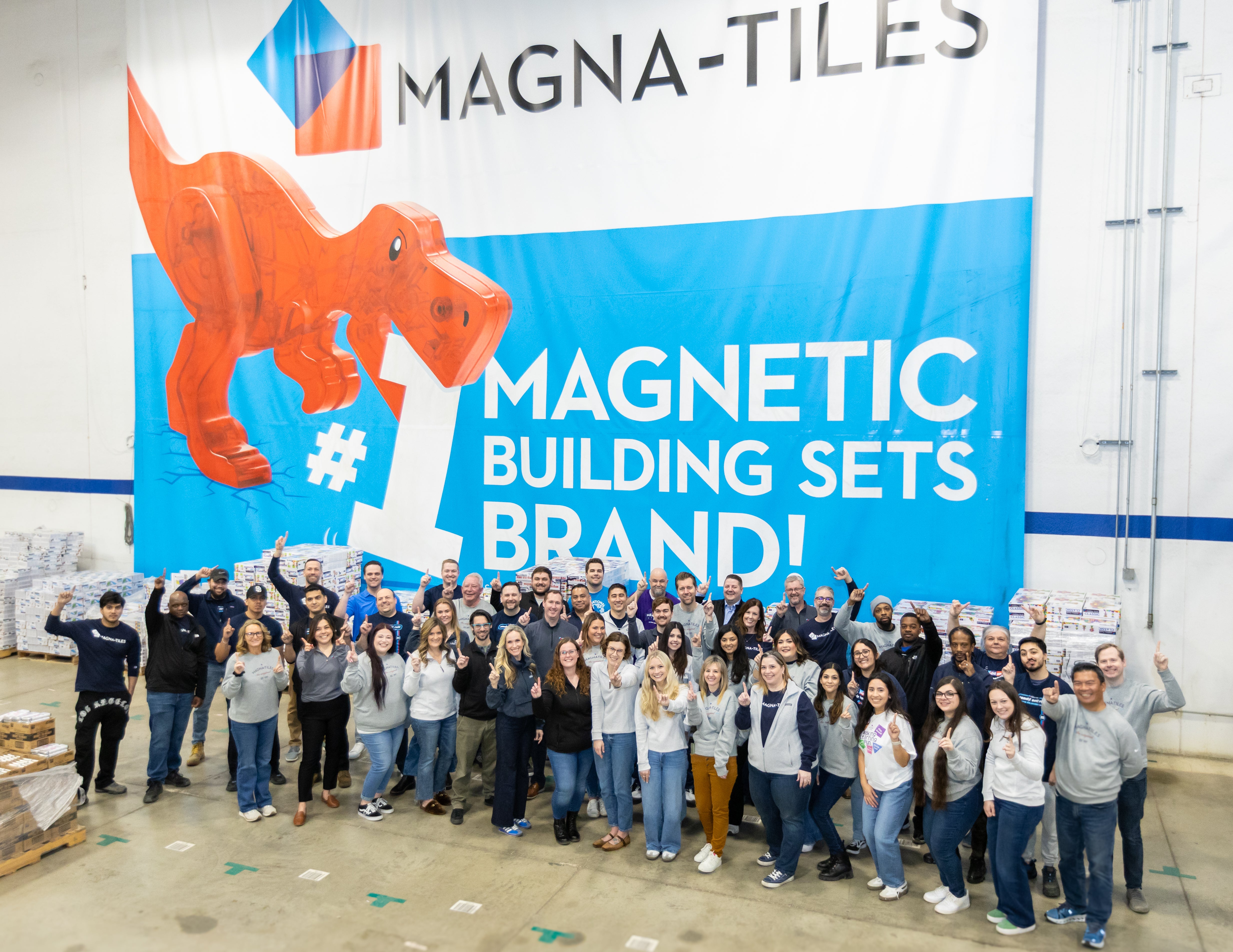 Group of Magna-Tiles employees holding up one finger in front of a banner that reads number one magnetic building sets