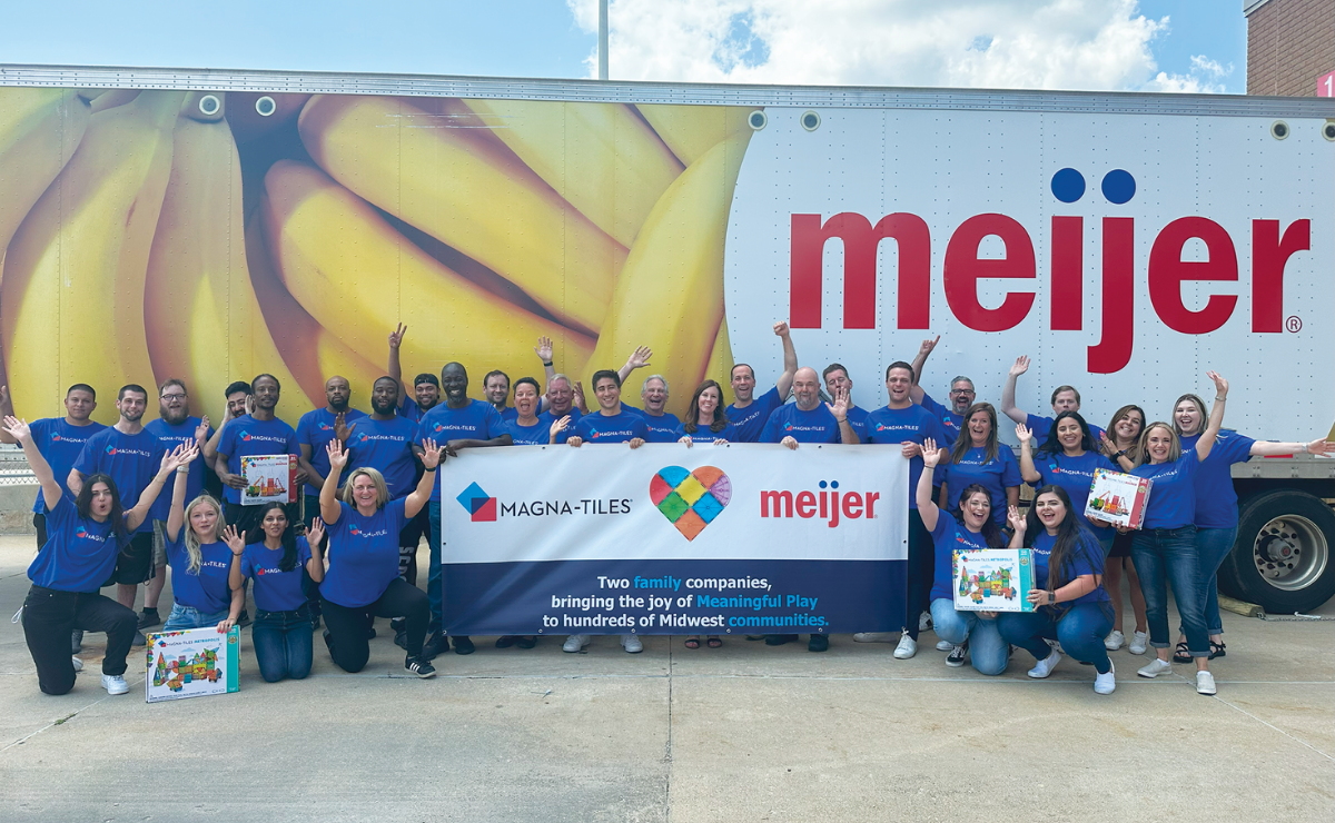 Magna-Tiles and Meijer employees in blue shirts holding a banner with both logos in front of a Meijer delivery truck