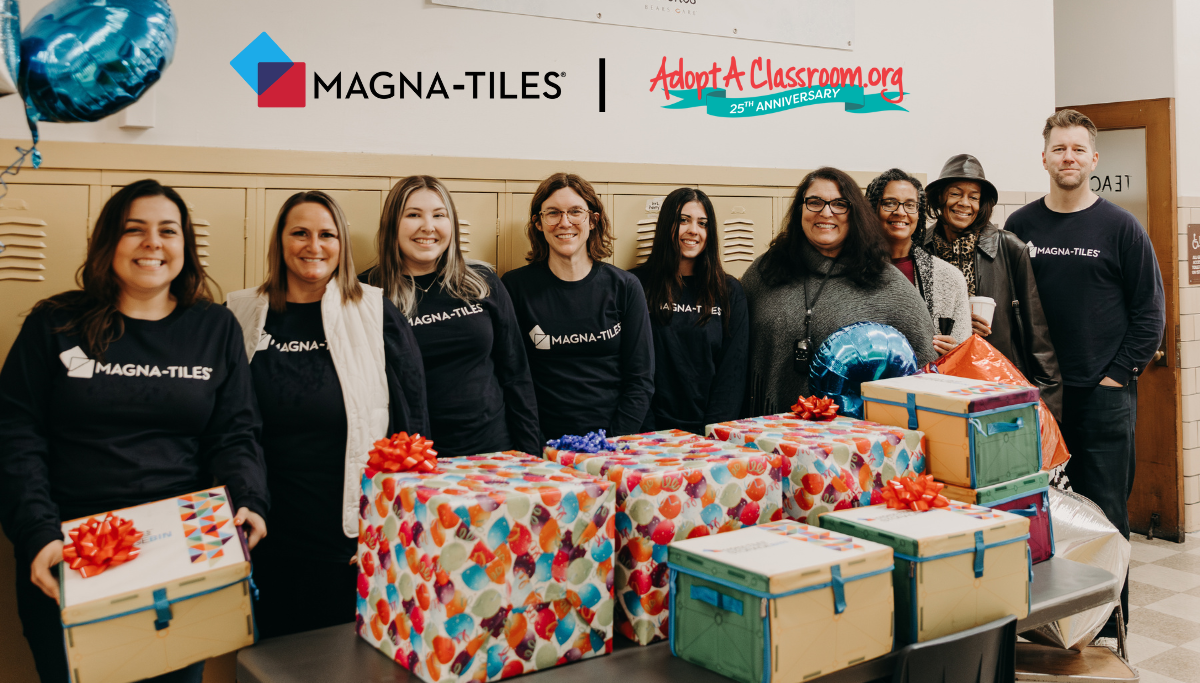 Magna-Tiles team posing with wrapped donation boxes in a school hallway under MAGNA-TILES and AdoptAClassroom.org 25th Anniversary logos