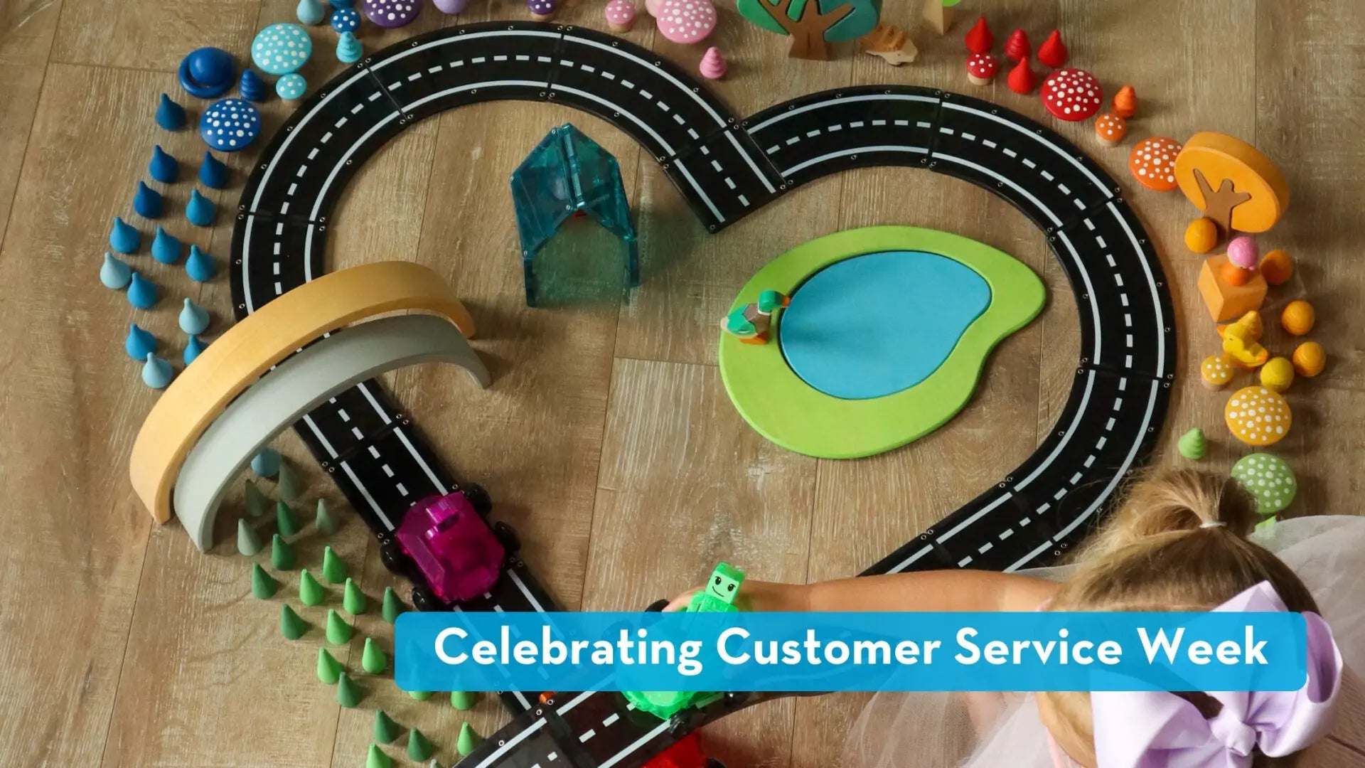 Overhead of a child playing with Magna-Tiles and a heart-shaped toy road; banner reads 'Celebrating Customer Service Week'