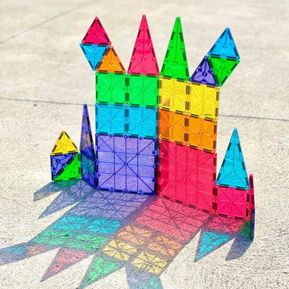 Front view of MAGNA-TILES Classic 37-piece set assembled into colorful towers and triangles on concrete with rainbow shadows