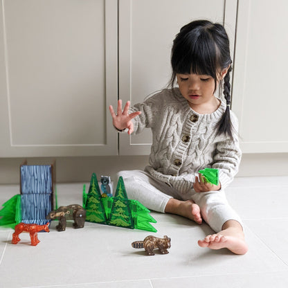 Child playing with MAGNA TILES Forest Animals 25-piece set on tile floor, building trees and arranging animal figures
