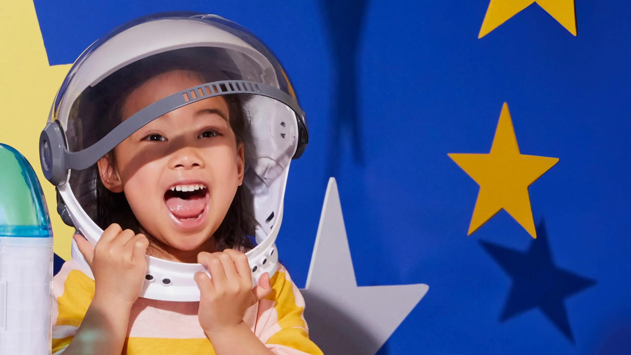 An excited child wearing a helmet in front of a background featuring stars